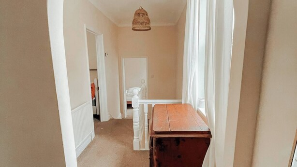 Un pasillo con un cofre de madera, cortinas blancas y una puerta blanca que da a otra habitación.