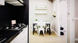 A kitchen with a stove, white cabinets, and a dining area with a table and chairs. - Beautiful apartment recently renovated and complete with everything (Roma)