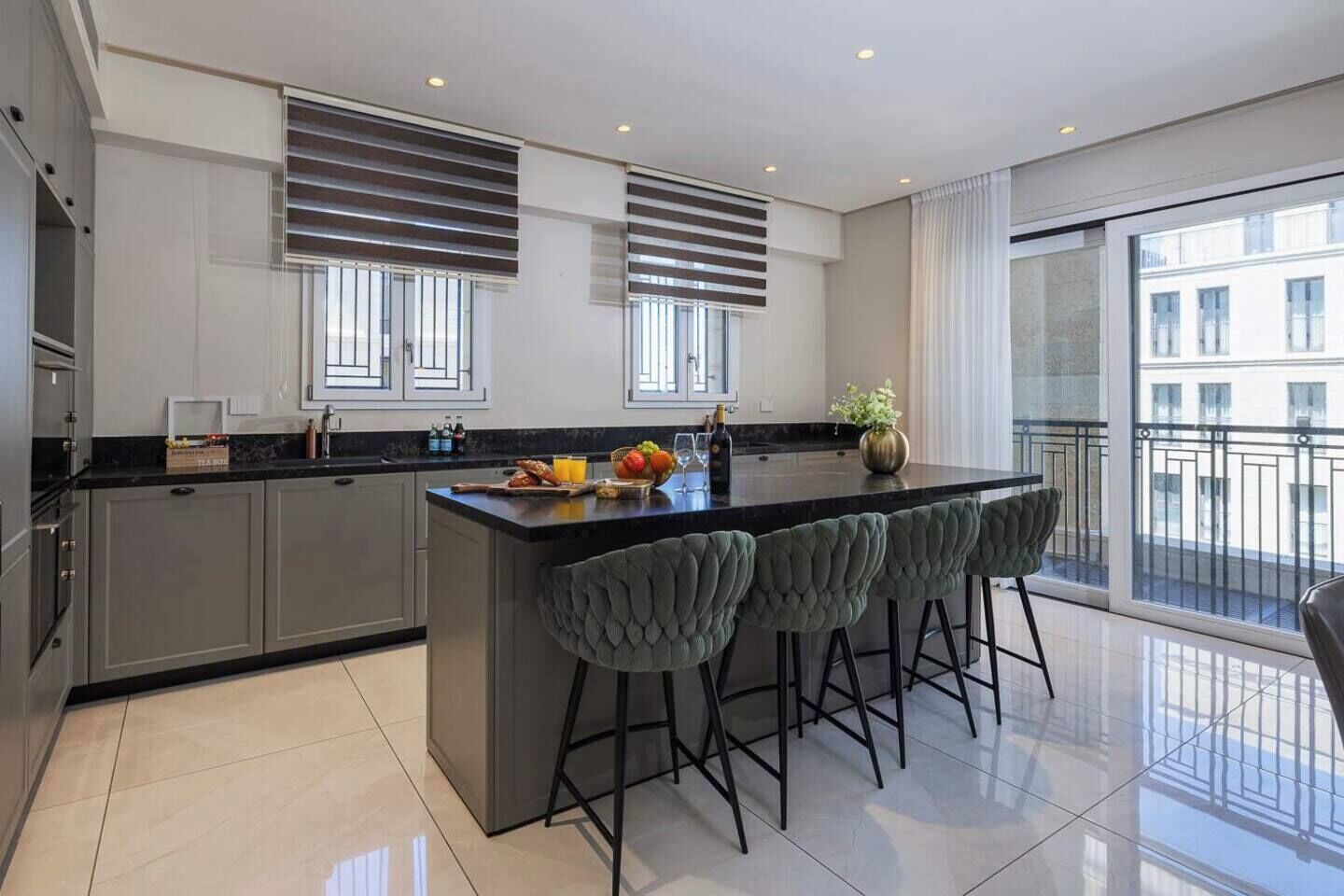 A modern kitchen with a central island, bar stools, and a view of the city through large windows.