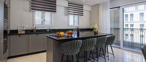 A modern kitchen with a central island, bar stools, and a view of the city through large windows.