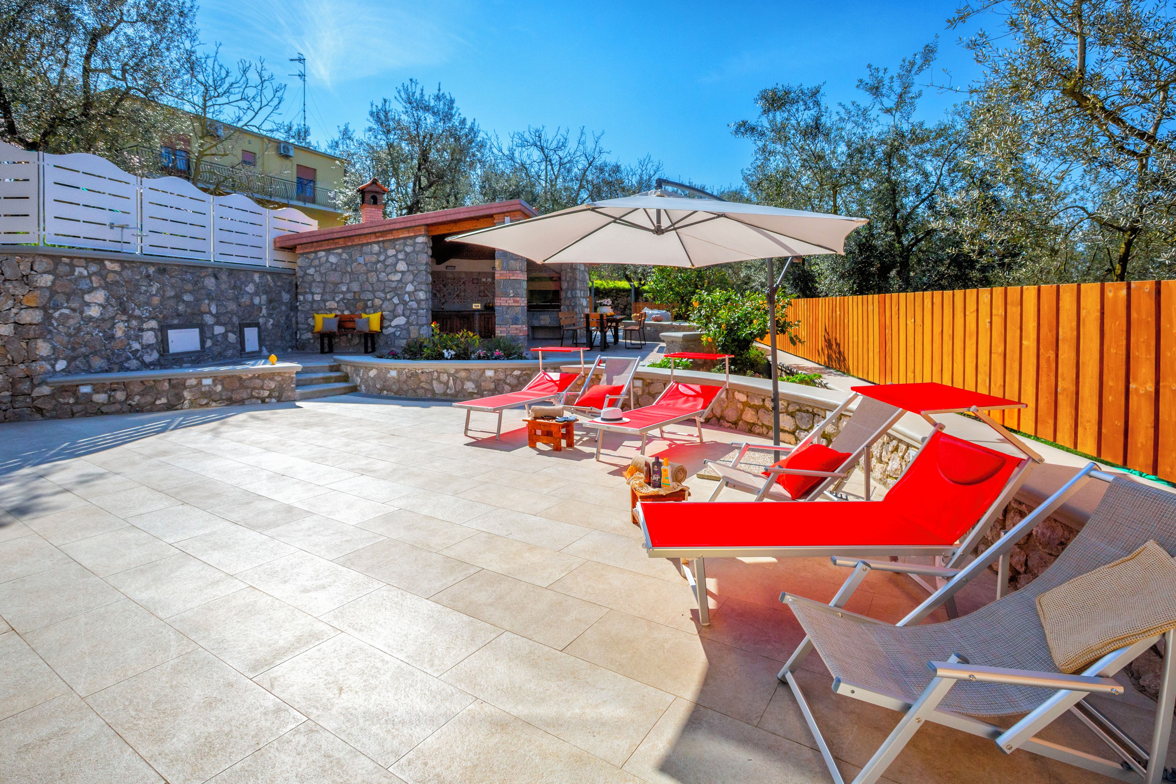 A patio area with stone walls, a barbecue, and outdoor seating with umbrellas.