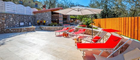 Un patio con muros de piedra, una parrilla y mobiliario exterior con sombrillas.