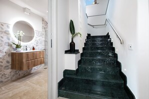 Un escalier avec une rampe menant à un palier, un meuble en bois avec des tiroirs, un miroir et une plante en pot.