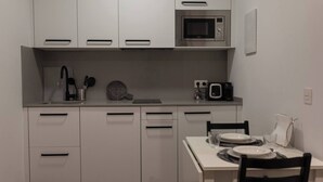 Une cuisine compacte avec des meubles blancs, un four à micro-ondes, un grille-pain et une table à manger avec des chaises.