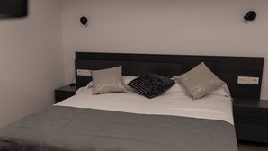 Un lit bien fait, avec une couverture grise et des coussins décoratifs, une tête de lit sombre et des tables de chevet avec des lampes.