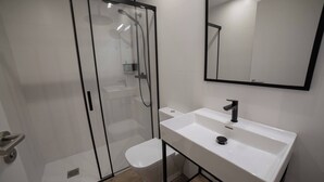 Une salle de bain moderne avec une douche à parois de verre, un lavabo blanc et un grand miroir.