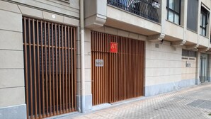 La façade d’un immeuble présente une entrée fermée par un portail, une enseigne indiquant « HATOR », et un balcon visible avec une rambarde en métal.