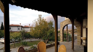 Ein überdachter Außenbereich mit Korbstühlen und einem Glastisch, mit Blick auf einen Garten und eine Steinbrücke.