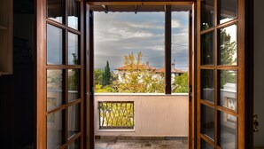 Ein offenes Durchgang führt zu einem Balkon mit Blick auf ein Gebäude mit roten Ziegeldächern und Bäumen.