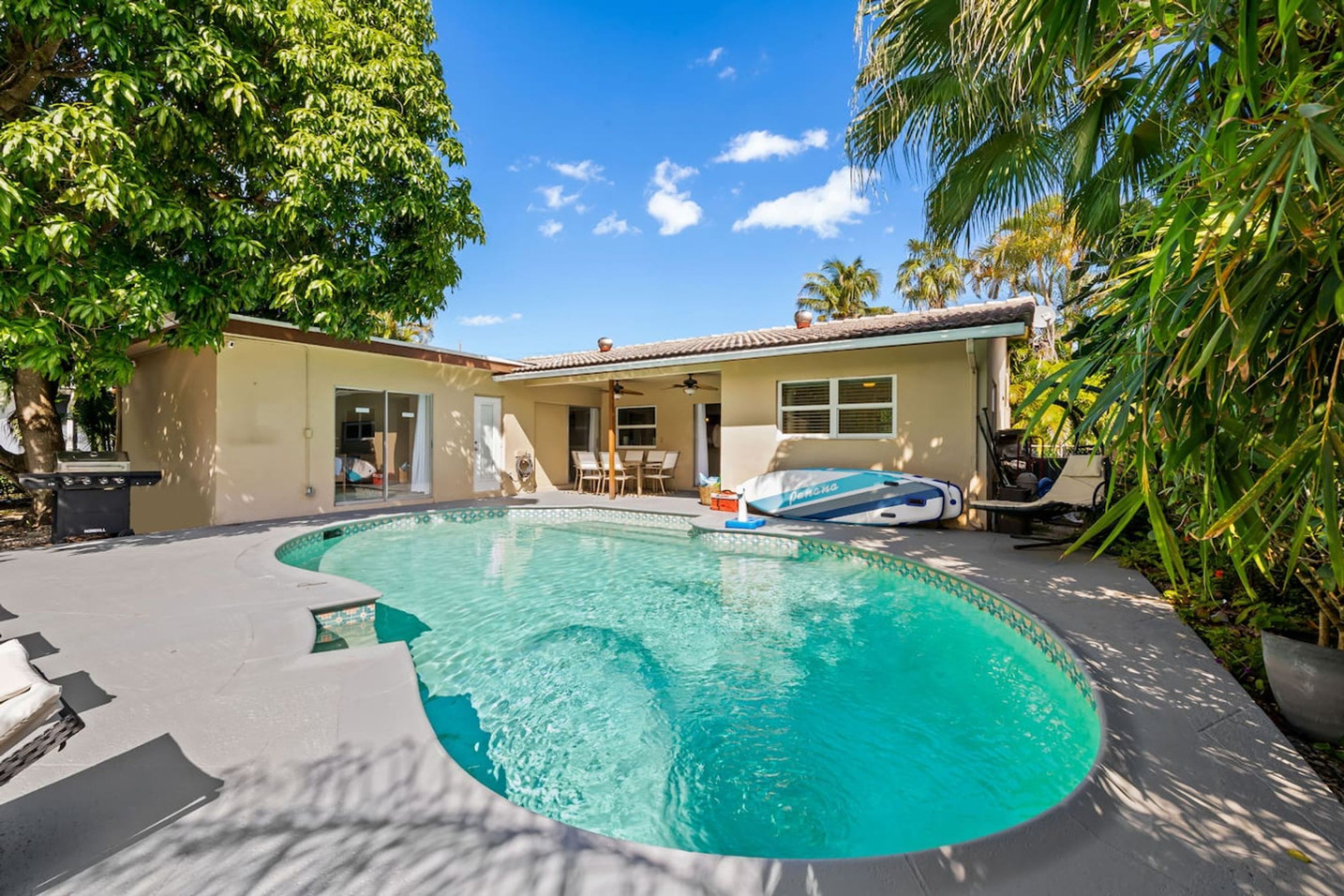 A swimming pool with a curved edge, surrounded by a patio area with lounge chairs and a covered seating area.