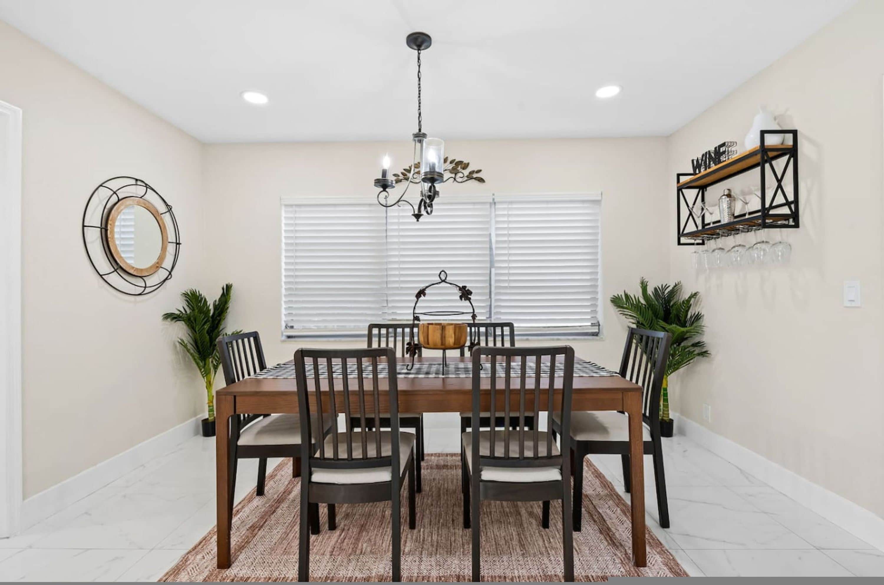 A dining room with a wooden table, six chairs, a chandelier, a mirror, and a wine rack.