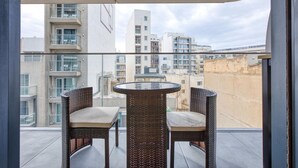 Un balcone con sedie in vimini e un tavolo di vetro, con vista su un panorama urbano ricco di edifici.