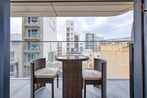 Ein Balkon mit Korbstühlen und einem Glastisch, mit Blick auf eine Stadtlandschaft mit mehreren Gebäuden.