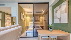 Una camera d'albergo moderna con un divano, un tavolo di legno con due sedie, un letto e un pannello di vetro.