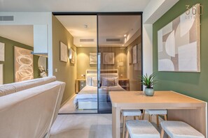 Ein modernes Hotelzimmer mit einer Couch, einem Holztisch mit zwei Stühlen, einem Bett und einer Glaskabine.