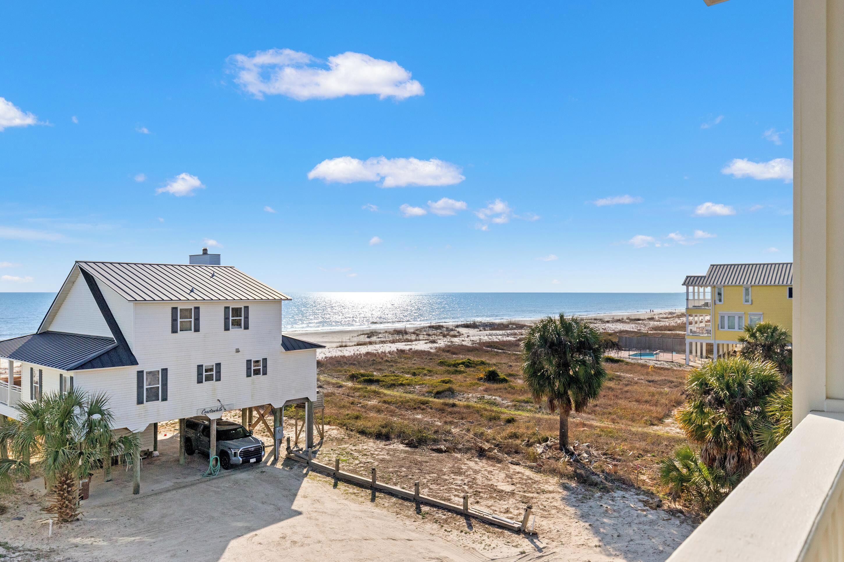 Een pand aan het strand met een wit huis, een geel huis en uitzicht op de oceaan.