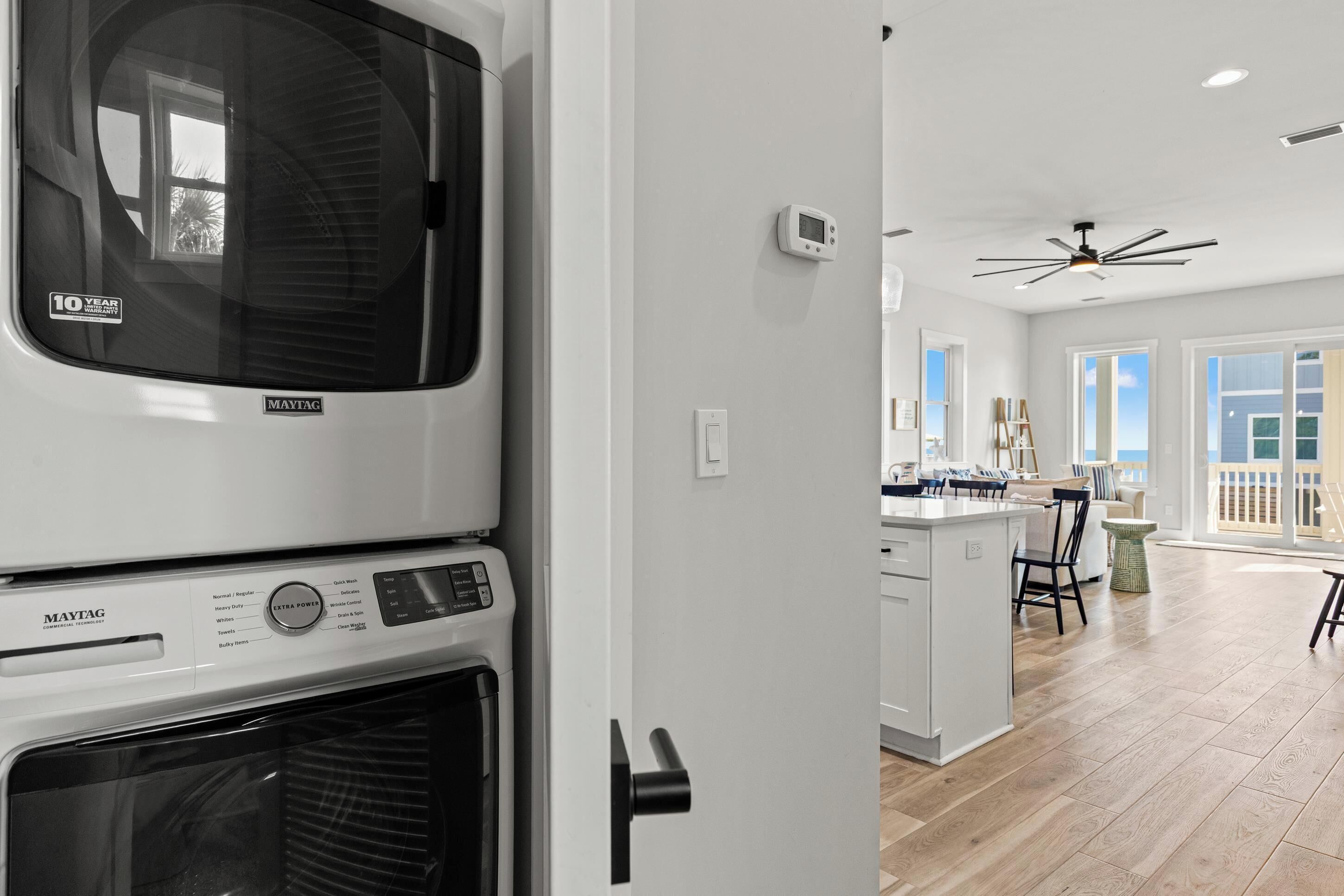 Una cocina moderna con lavadora y secadora integradas, un ventilador de techo y vistas al área de estar con juego de comedor.