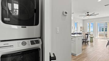 Una cocina moderna con lavadora y secadora integradas, un ventilador de techo y vistas al área de estar con juego de comedor.
