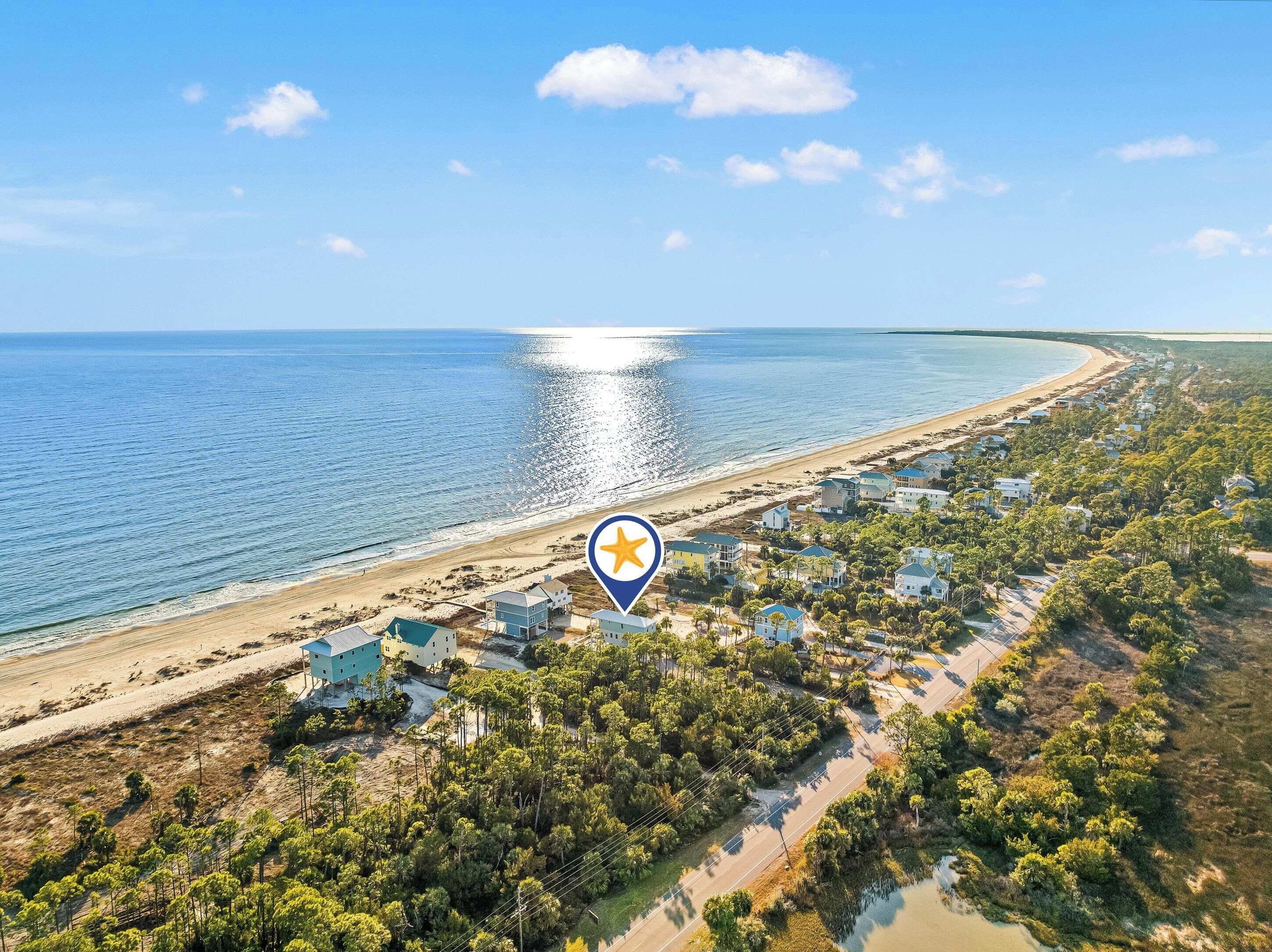 An aerial view of a coastal area with a beach, houses, and a road.