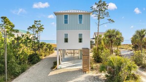 A two-story beach house with a gravel driveway and a wooden deck. - Pet Friendly Beach House - Bella View (Port St. Joe)