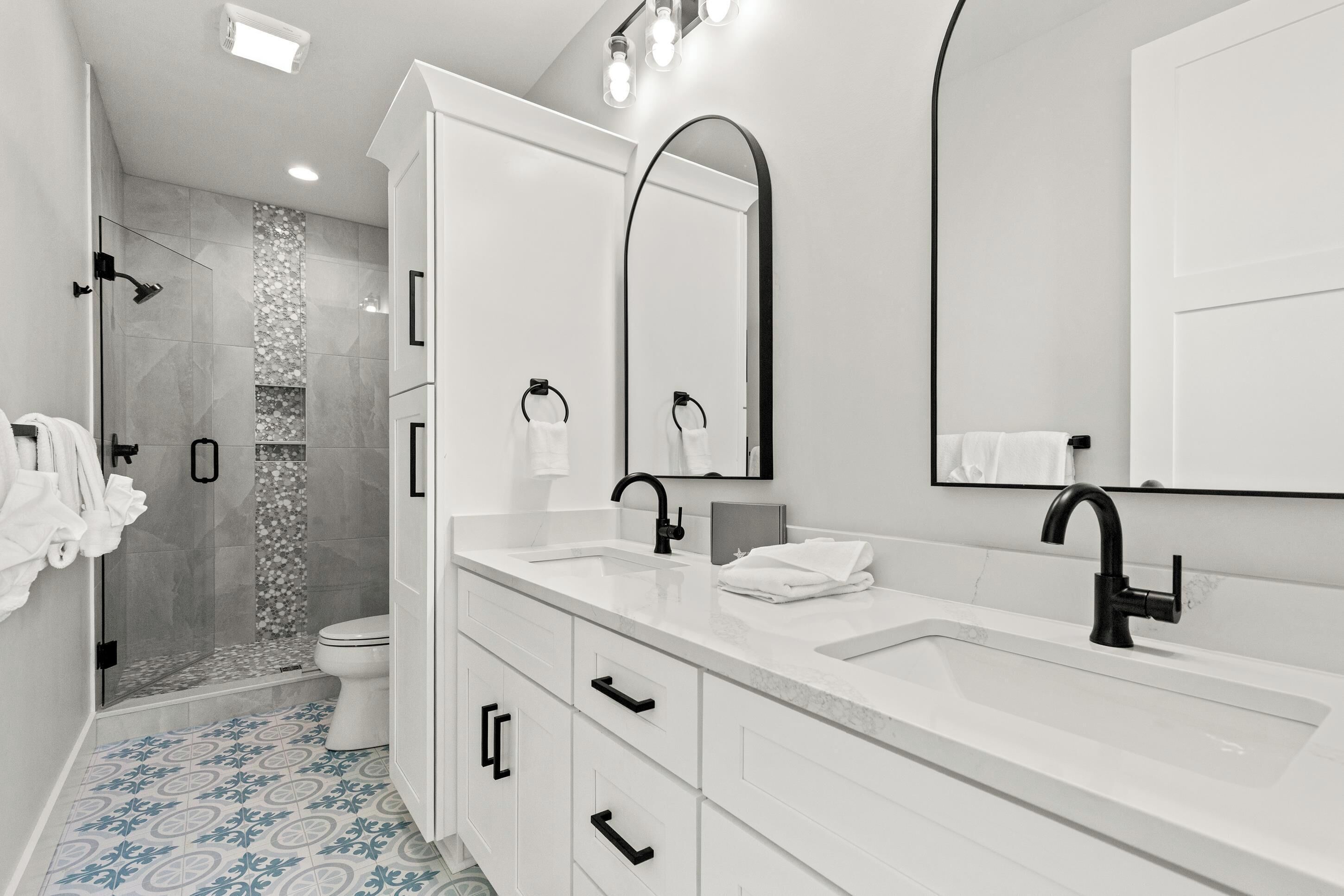 Un baño moderno con cabina de ducha, un espejo grande y un tocador blanco con lavabo y encimera.