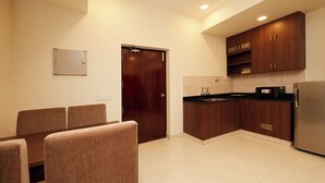 Una cocina moderna con armarios de madera oscura, un refrigerador de acero inoxidable y un comedor con sillas tapizadas en tono marrón.