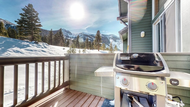 Eine Holzterrasse mit Grill und Blick auf schneebedeckte Berge.