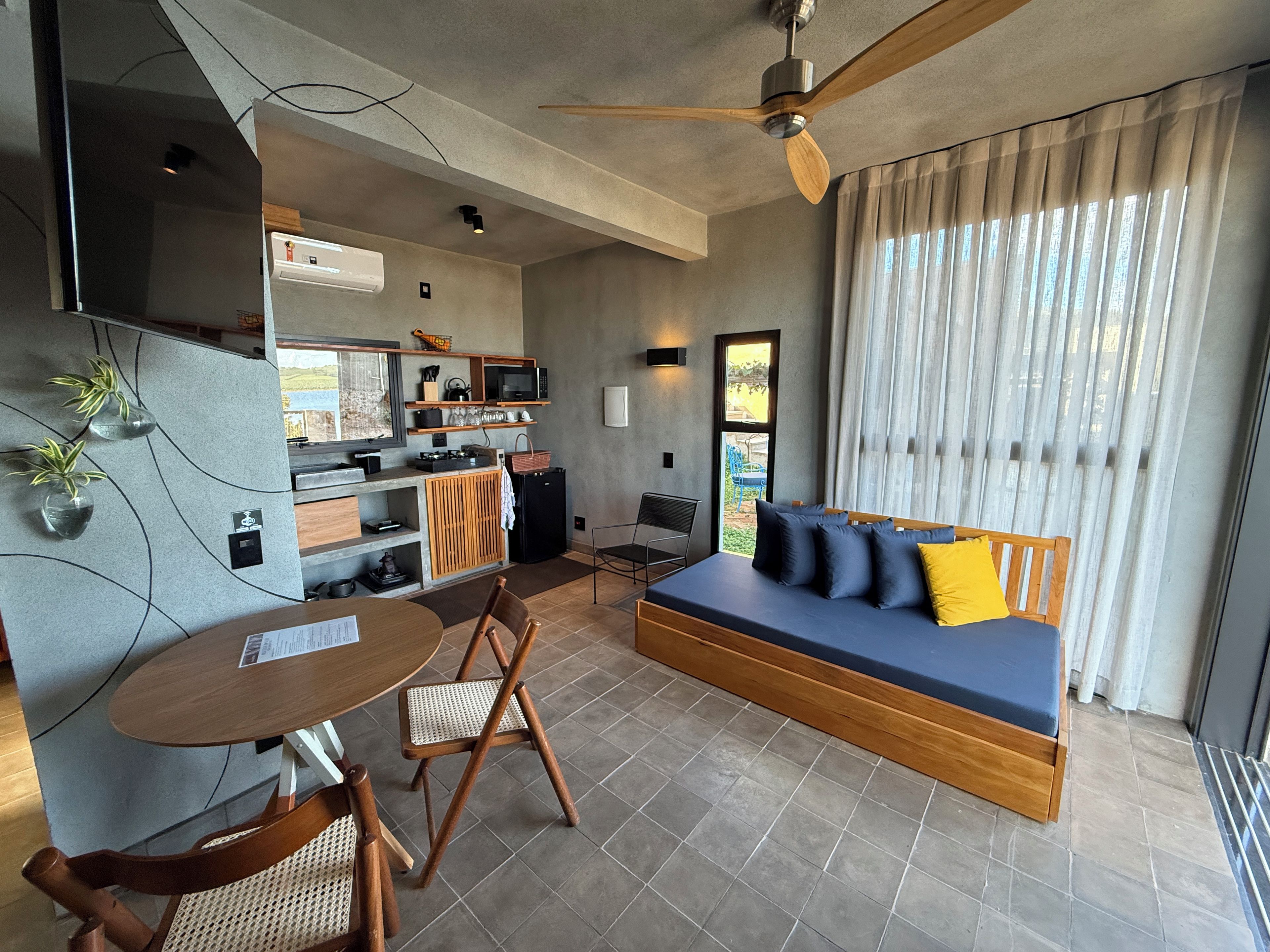 A modern living space with a sofa, dining table, chairs, kitchenette, and a ceiling fan.