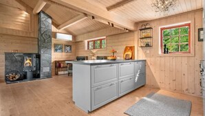 A wooden cabin interior with a stone fireplace, a kitchen island, and a window with a view of greenery.