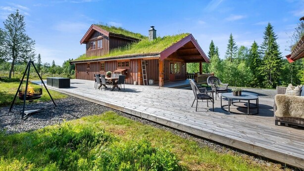 A wooden cabin with a green roof, a deck with outdoor furniture, and a fire pit.