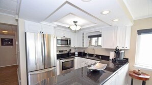 A modern kitchen with stainless steel appliances, a granite countertop, and white cabinetry. - Thunder Island 13a 2 Bedroom Condo (Ocean City)