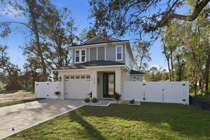A two-story house with a garage, surrounded by a white fence, and a well-maintained lawn with small plants. - Modern Mount Dora Escape Style And Sunshine 4 Bedroom Home (Mount Dora)