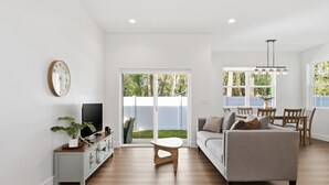 Ein modernes Wohnzimmer mit einer Couch, einem Fernseher und einem Essbereich mit Tisch und Stühlen.