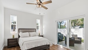 Ein Schlafzimmer mit einem großen Bett, Holzboden, Deckenventilator und einer Glasschiebetür, die zu einem Außenbereich führt.