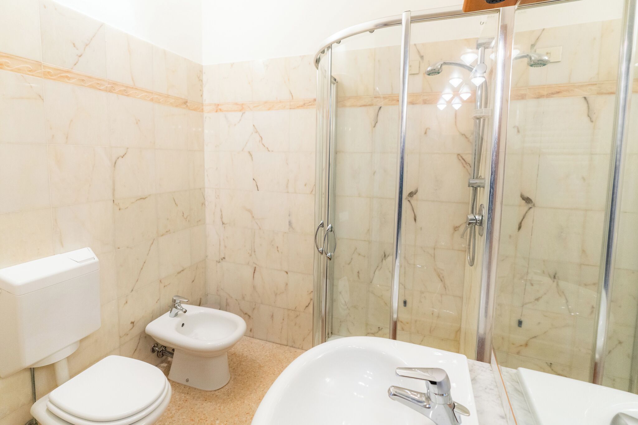 A bathroom with a glass-enclosed shower, a toilet, and a sink.