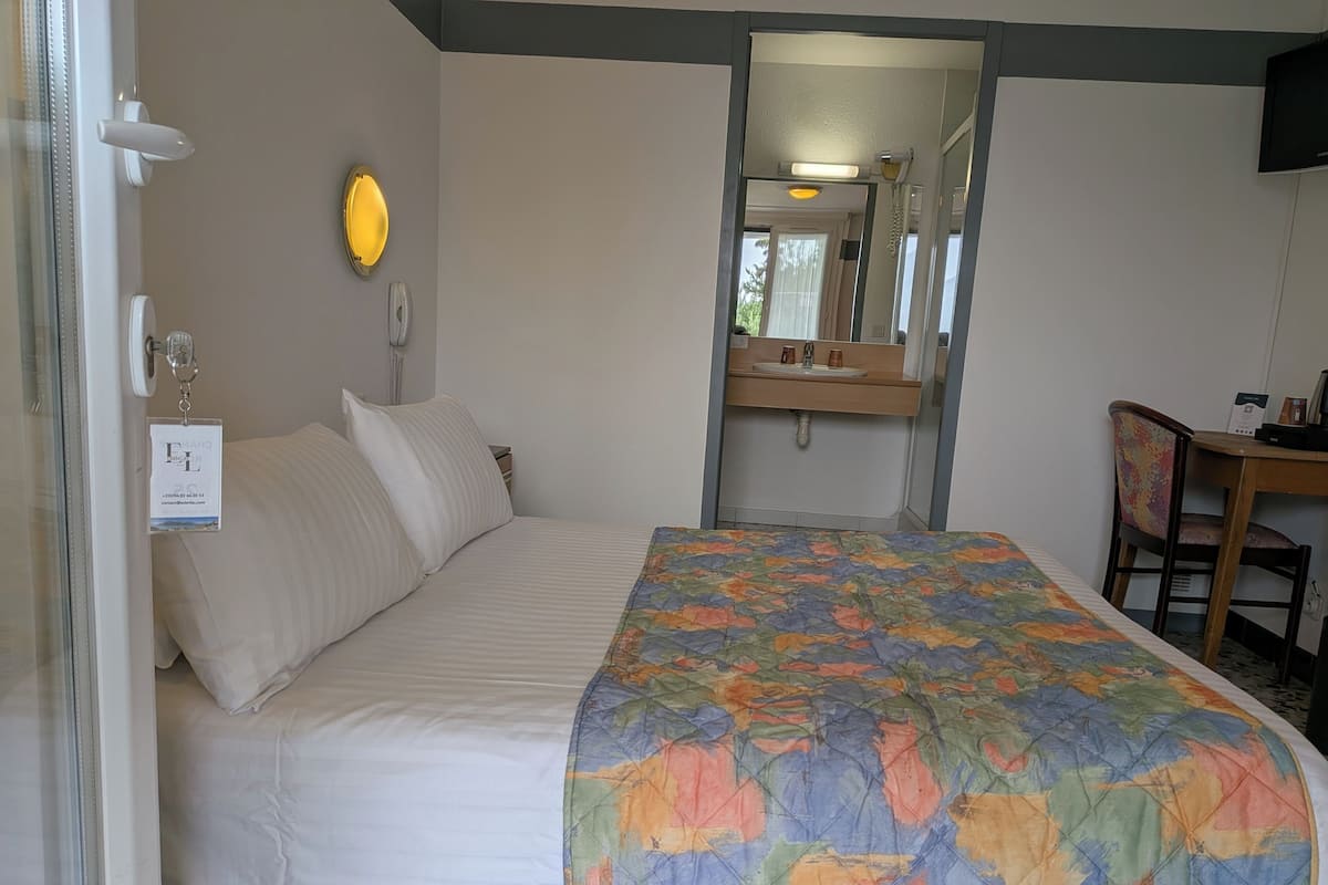 A hotel room with a bed, a desk, a chair, a mirror, and a window.