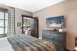 Een slaapkamer met een groot raam, een deur, een dressoir en een schilderij aan de muur.