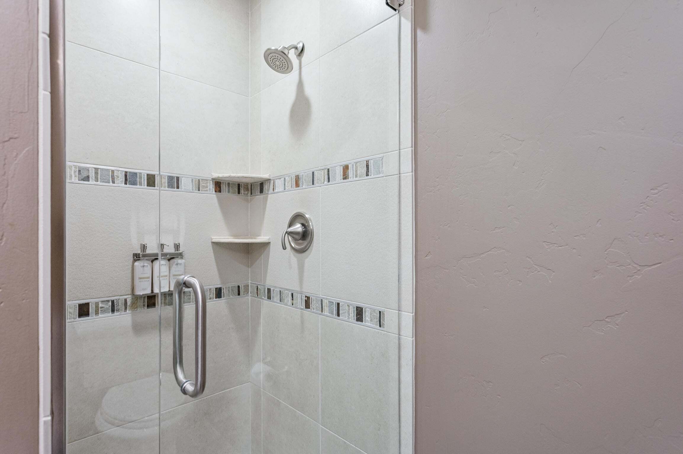 A shower with a handheld showerhead, a glass door, and a tiled wall with a decorative border.