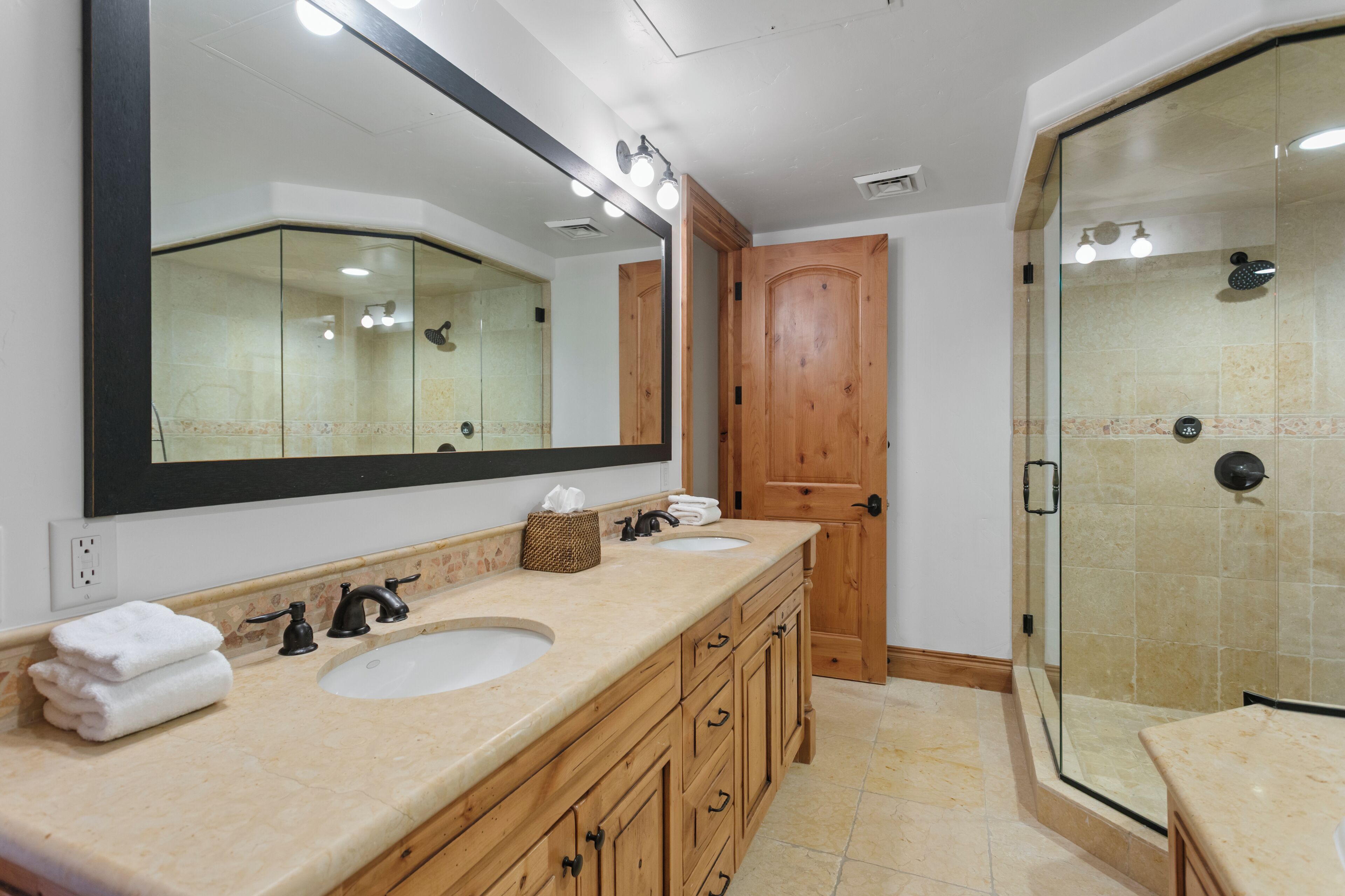 Une salle de bain avec deux lavabos, un grand miroir et une douche fermée par une paroi de verre.