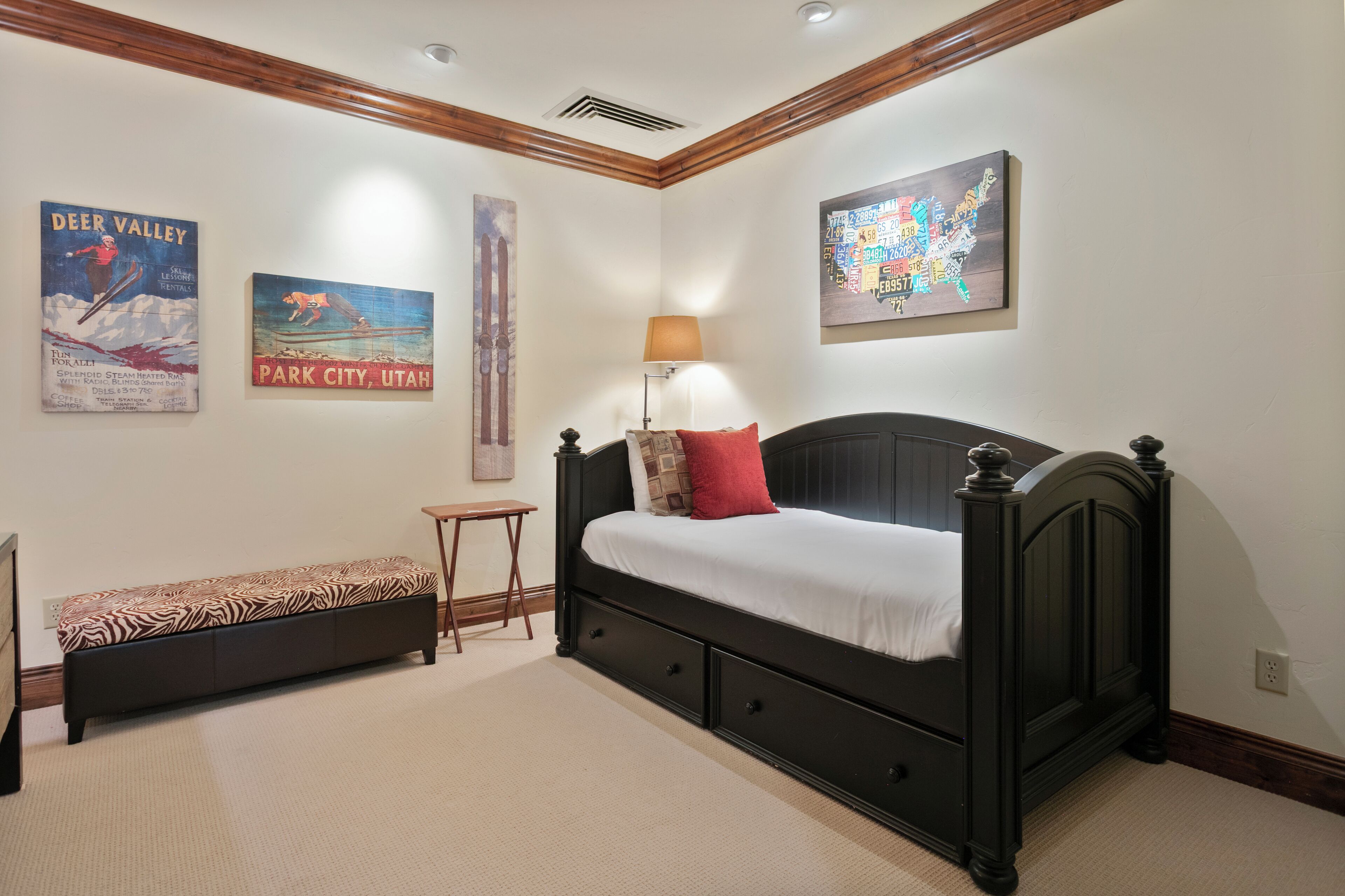 A bedroom with a bed, a bench, a lamp, and wall art including a map and posters.