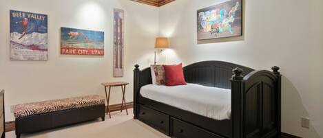 A bedroom with a bed, a bench, a lamp, and wall art including a map and posters.