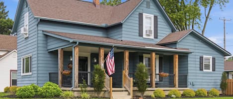 A two-story house with a front porch, a chimney, and an American flag.