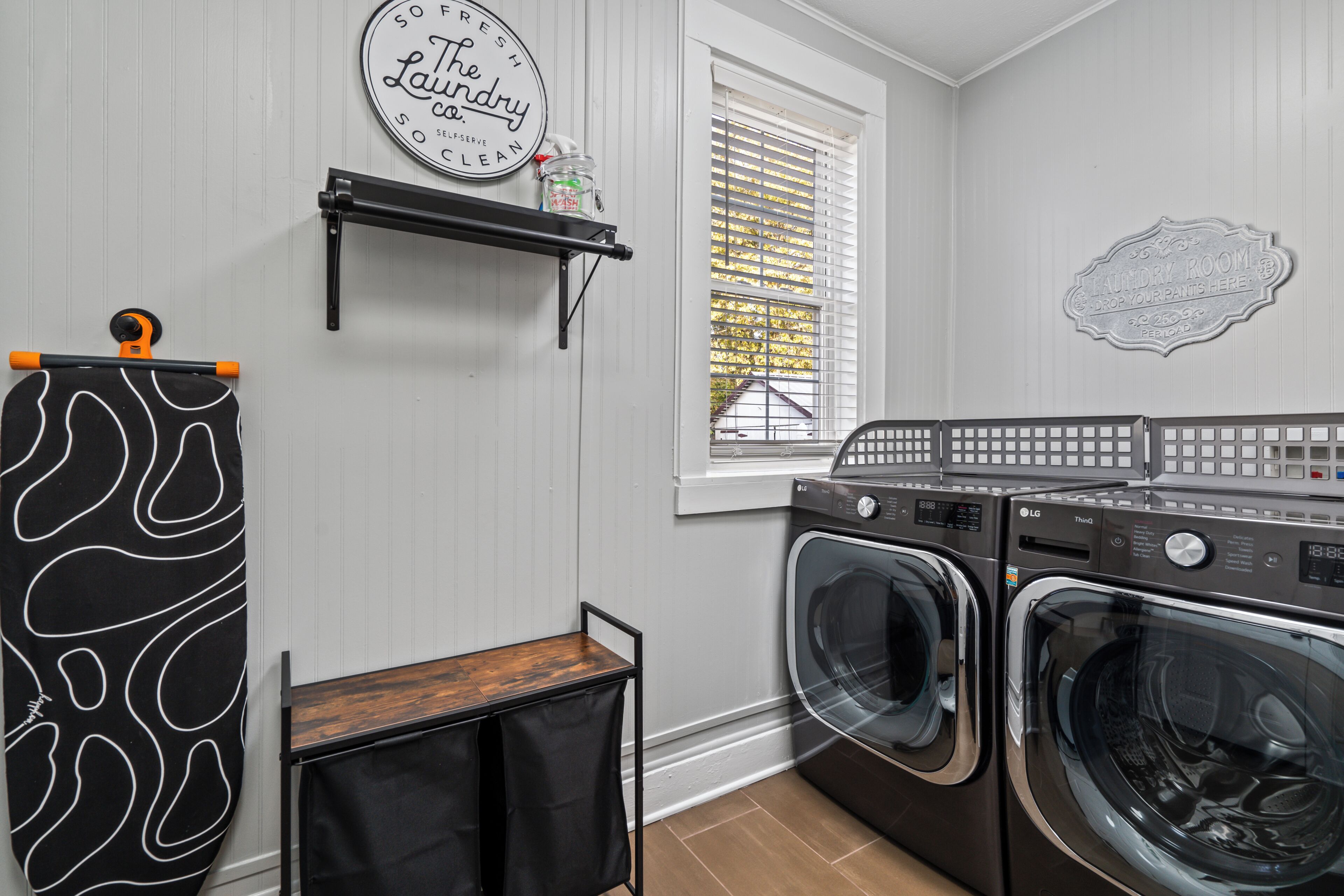 A laundry room with two front-loading washers and dryers, a shelf with laundry supplies, and a wall-mounted sign.