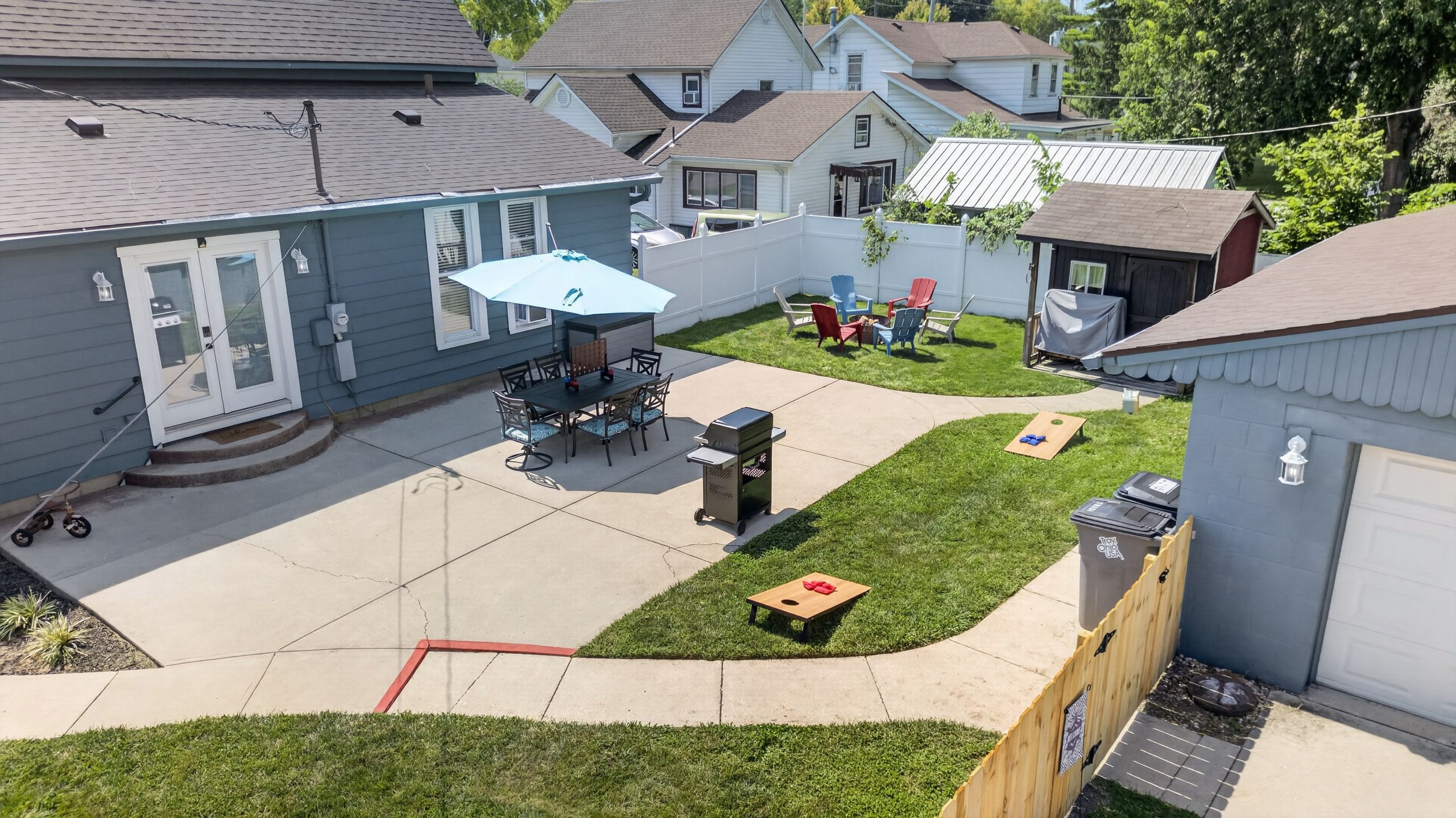 A residential backyard with a patio, outdoor seating, a grill, and a fenced play area.