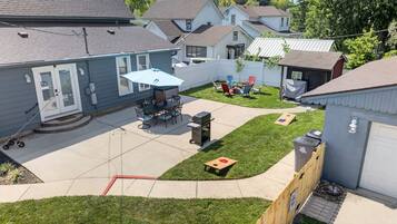 A residential backyard with a patio, outdoor seating, a grill, and a fenced play area.
