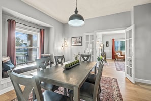 A dining area with a wooden table, chairs, a chandelier, and a view through an open door.