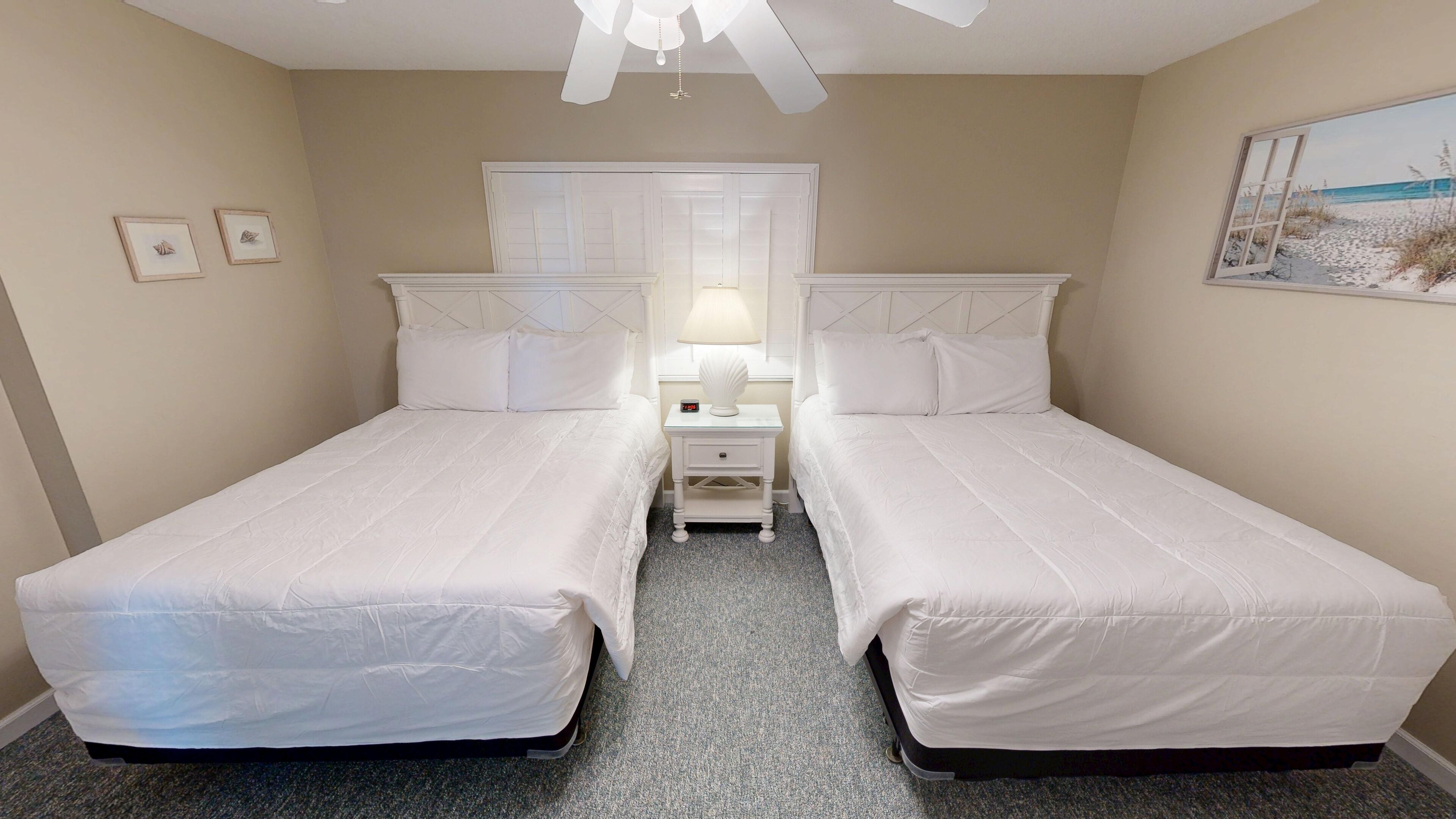 A twin bedroom with two beds, a nightstand with a lamp, and a window with a beach view.