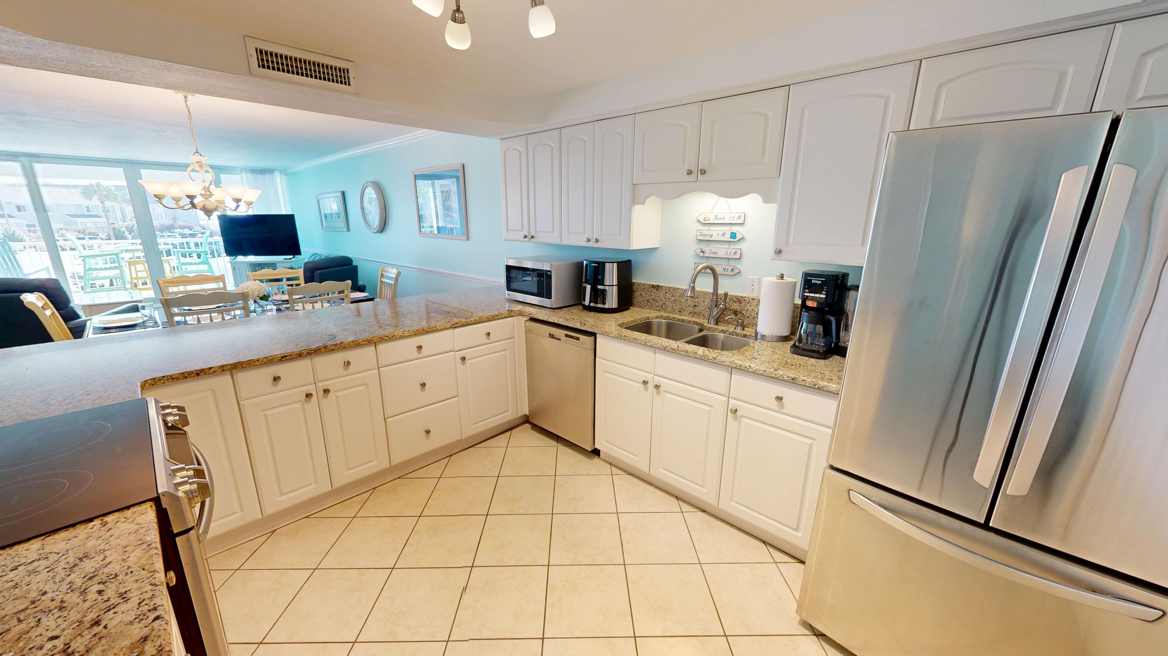 A modern kitchen with white cabinets, a stainless steel refrigerator, a dishwasher, and a granite countertop.