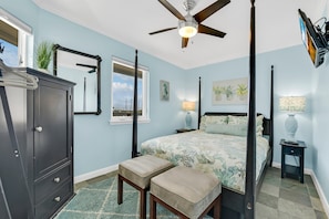 A bedroom with a four-poster bed, a ceiling fan, a dresser, and a view of the sky through a window. - Seascape 1119 1 Bedroom Condo (Galveston)