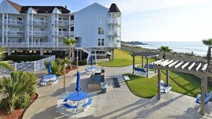 Ein Strandhotel mit mehreren Balkonen, Sitzgelegenheiten im Freien und einem Poolbereich.
